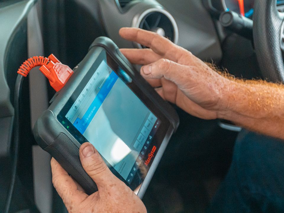 Mechaniker hält ein Diagnosegerät, das per Kabel mit dem Auto verbunden ist